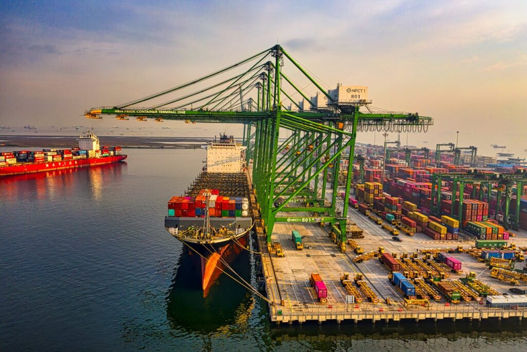 A bustling aerial view of a container port in North Jakarta, Indonesia with ships and cranes.